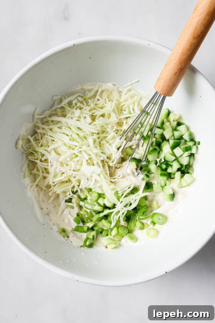 Chopped cabbage, green onions and cucumbers in a bowl with a whisk.