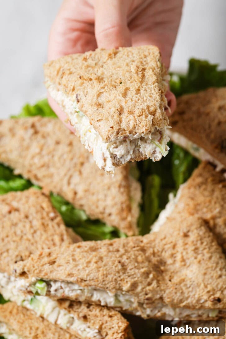 Holding a partially eaten Chicken Sandwich over a platter of sandwiches.