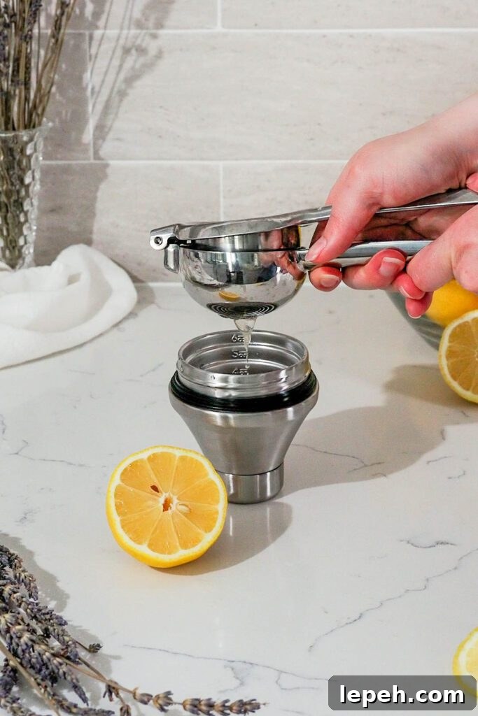 A lemon is squeezed over a jigger with a lemon squeezer.