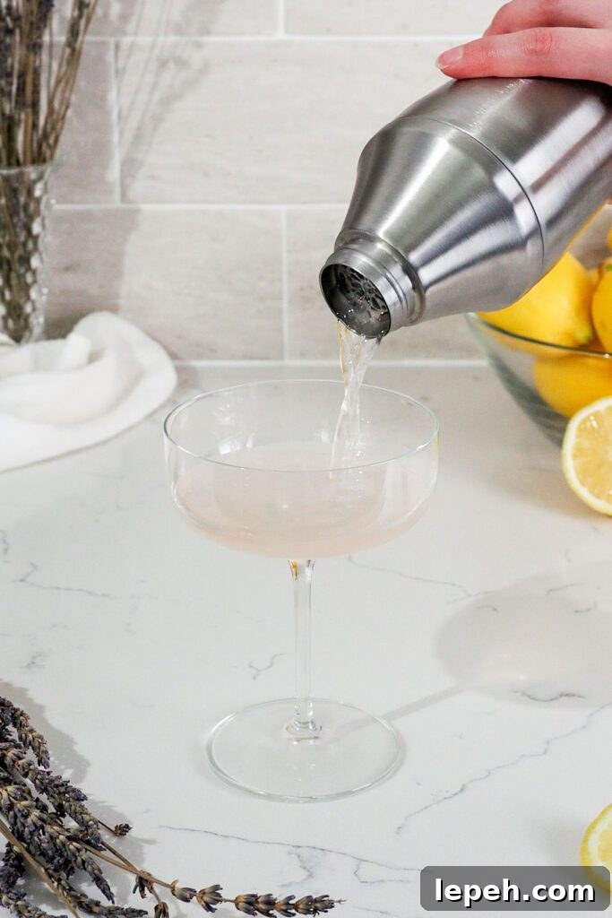 A pink cocktail is poured out of a shaker and into a coupe glass.