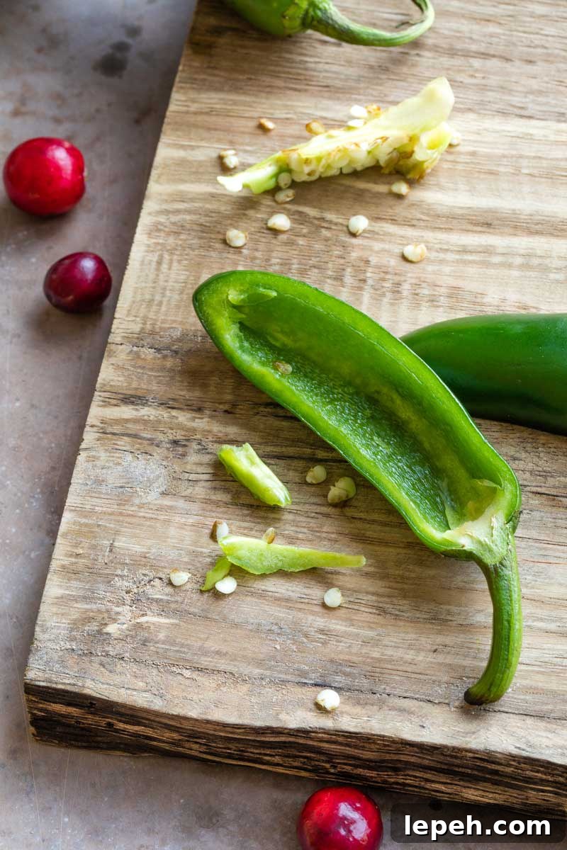 Halved jalapeno on cutting board with seeds and ribs removed and divided, and a couple cranberry nearby.