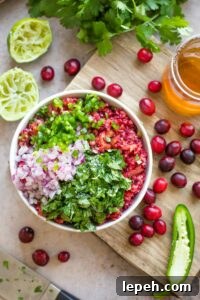 Overhead of bowl filled with cranberry mixture, with chopped onions, jalapeno and onion arranged on top and waiting to be mixed into the salsa.