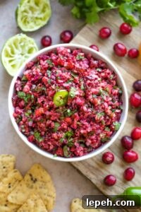 Overhead of finished salsa in bowl on cutting board, surrounded by extra ingredients.