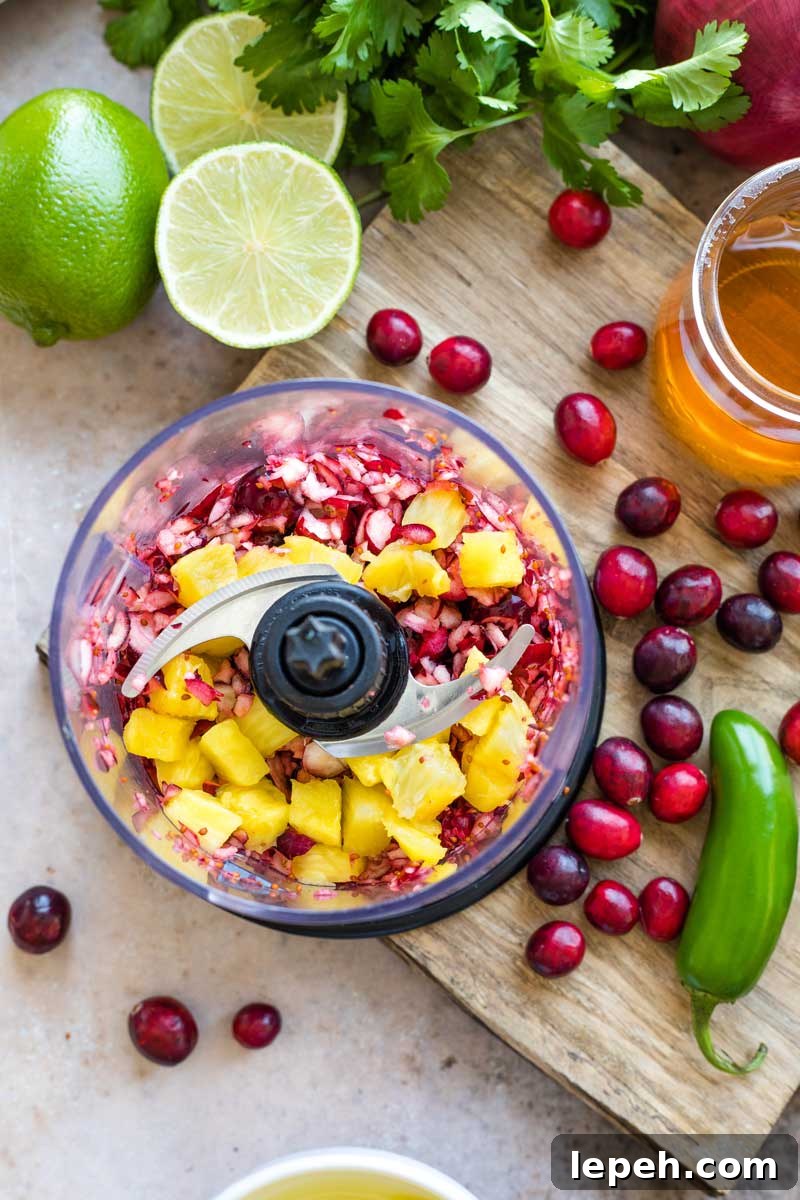 Overhead of processor with partially chopped cranberries and pineapple added on top.