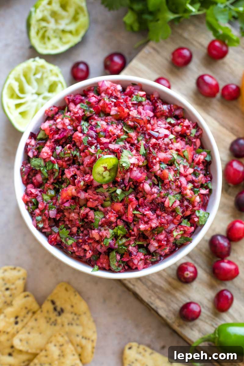 Overhead of finished salsa in bowl on cutting board, surrounded by extra ingredients.