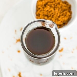 A glass bottle full of brown sugar simple syrup with a bowl of brown sugar next to it.
