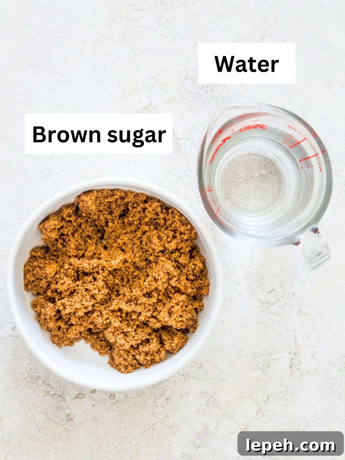 A white bowl filled with brown sugar and a glass measuring cup filled with water.