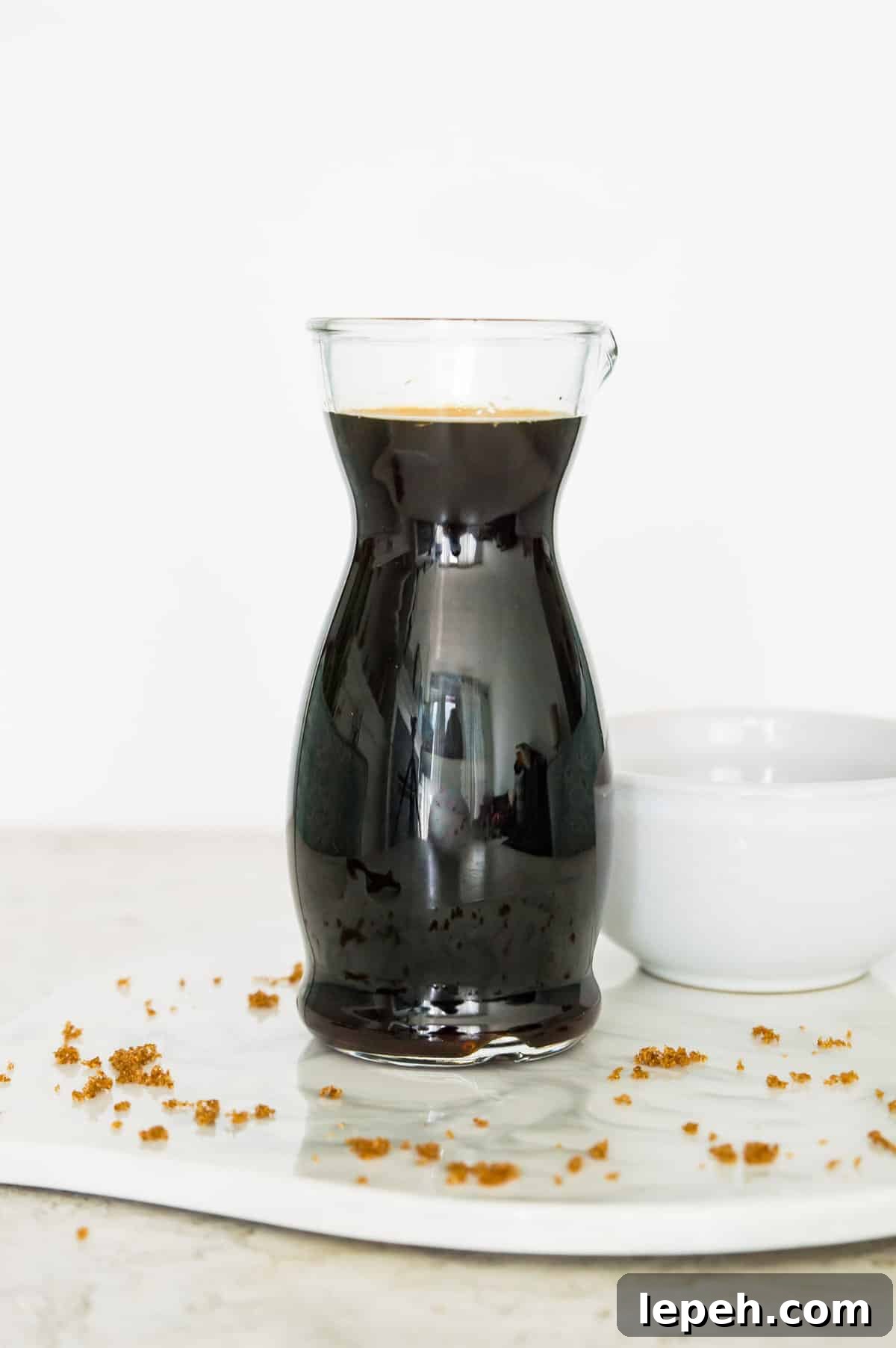A glass bottle filled with brown sugar syrup with a white bowl next to it.