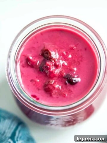 A jar of raspberry blueberry sauce surrounded by fresh blueberries.