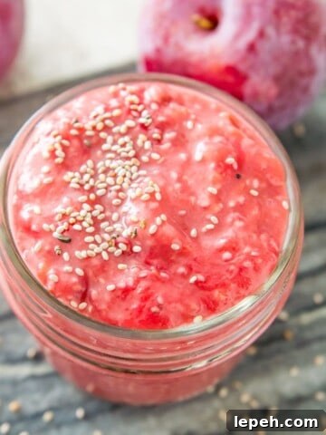 A jar of plum chia jam topped with chia seeds and two plums beside the jar.