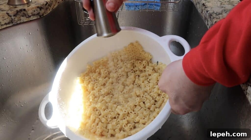 Rinsing cooked pasta under cold water in a colander in the sink