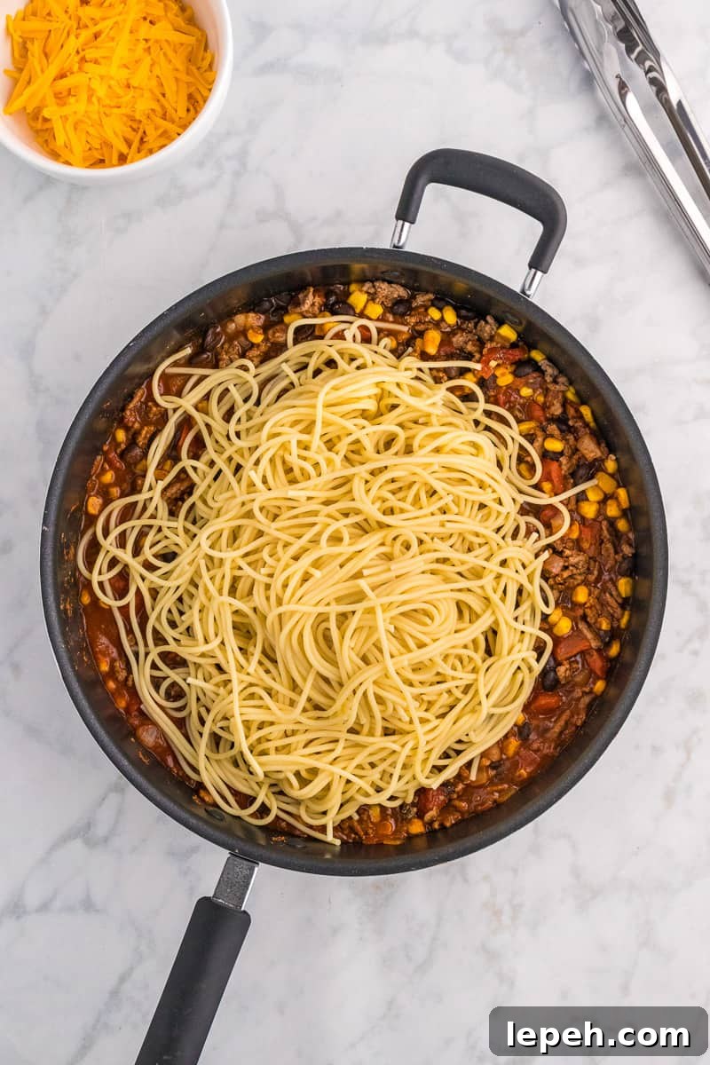 Spaghetti noodles are added to ground beef mixture for taco spaghetti.