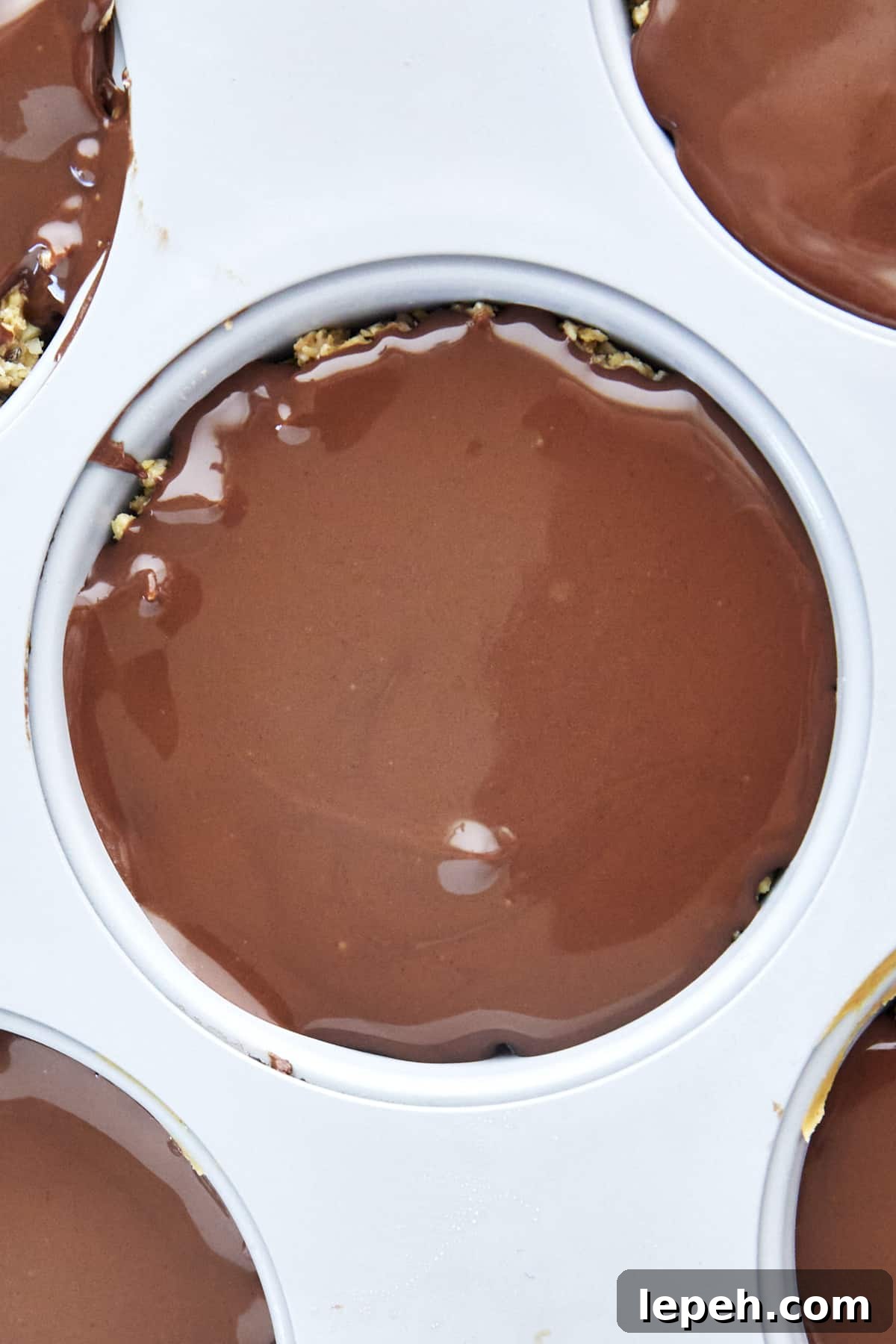 Chocolate covering a no bake peanut butter oat cup in a muffin pan. 