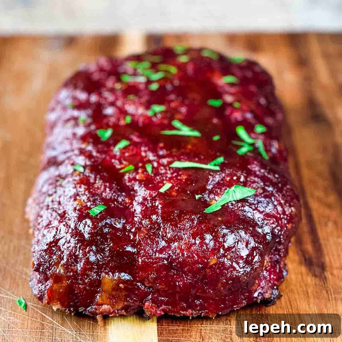 The barbecue glazed stuffed meatloaf on a wooden cutting board, garnished with fresh parsley.