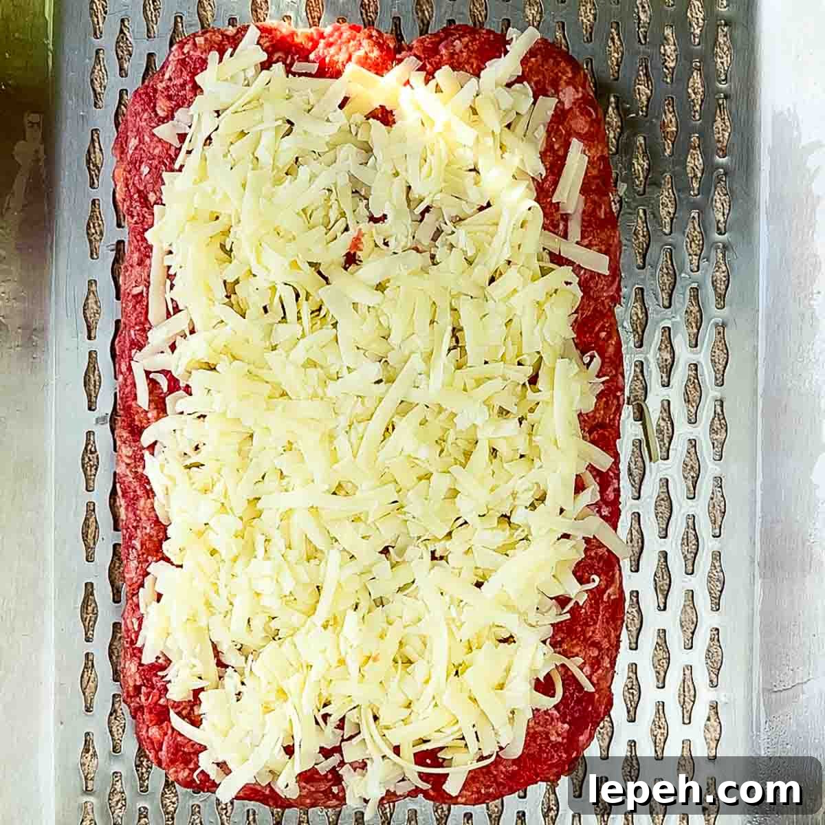 Half of the meat mixture formed into a loaf shape with shredded cheese on top.