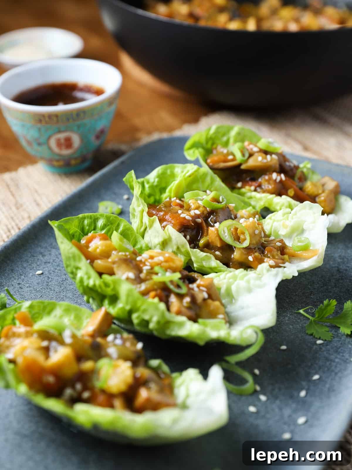 Photo of a grey-blue oblong plate with 4 little gem lettuce leaves filled with vegan san choy bau filling and a bowl of hoisin sauce to top them with.