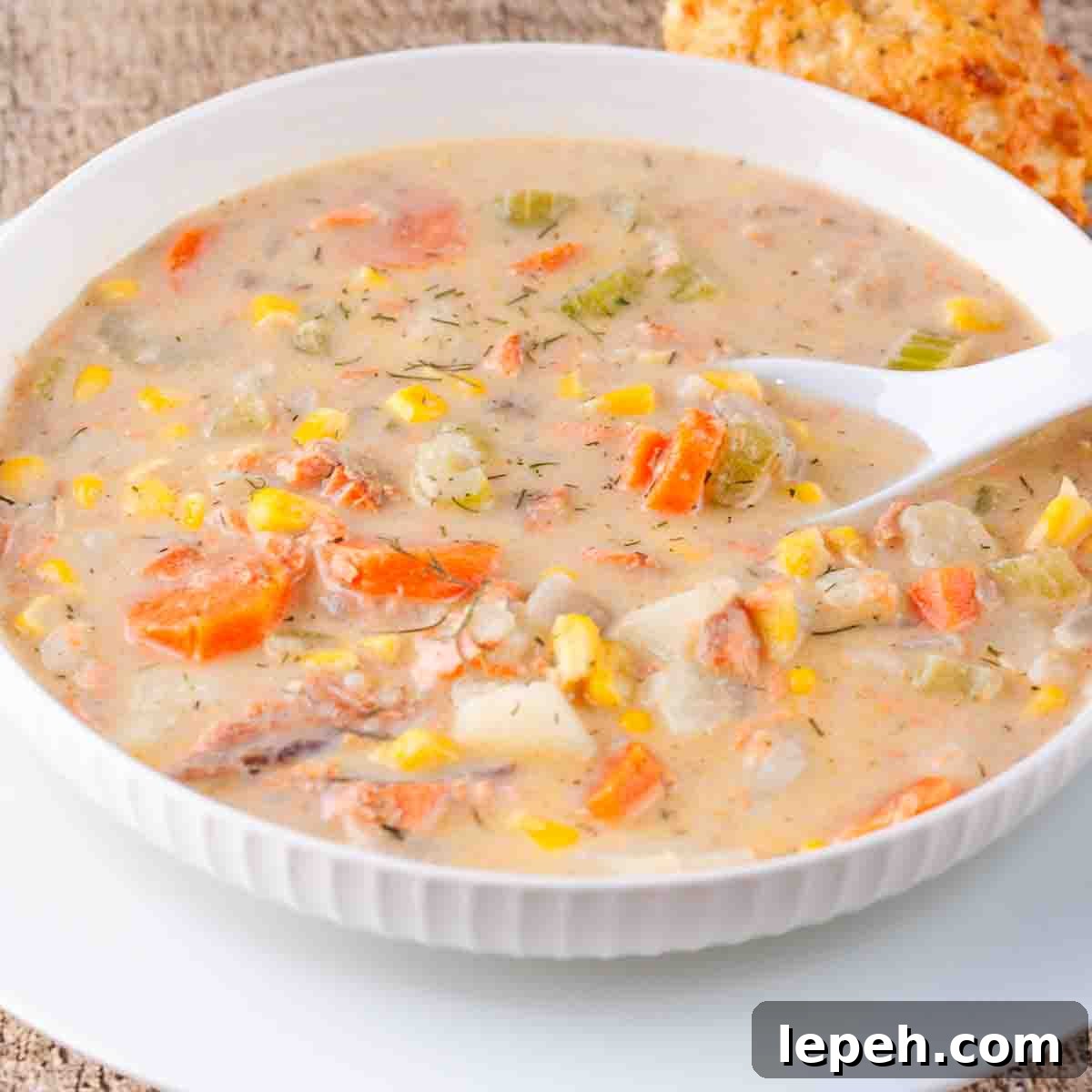 A white bowl filled with seafood chowder, with a cheese biscuit on the side.