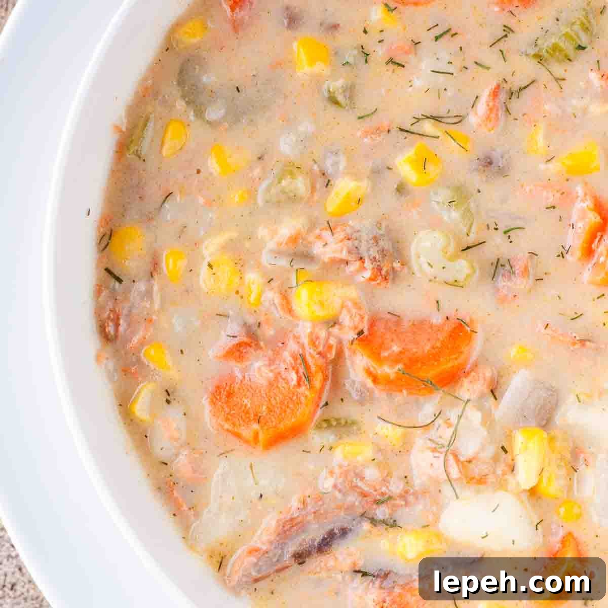 A white soup spoon in a bowl of seafood chowder with a biscuit on the side.