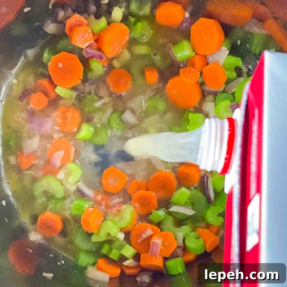 Chicken stock being added to the instant pot with the vegetables.