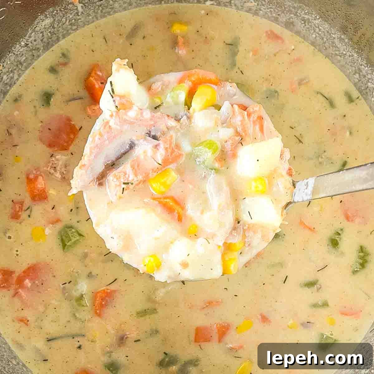 A soup ladle lifting up a spoonful of salmon chowder for serving.