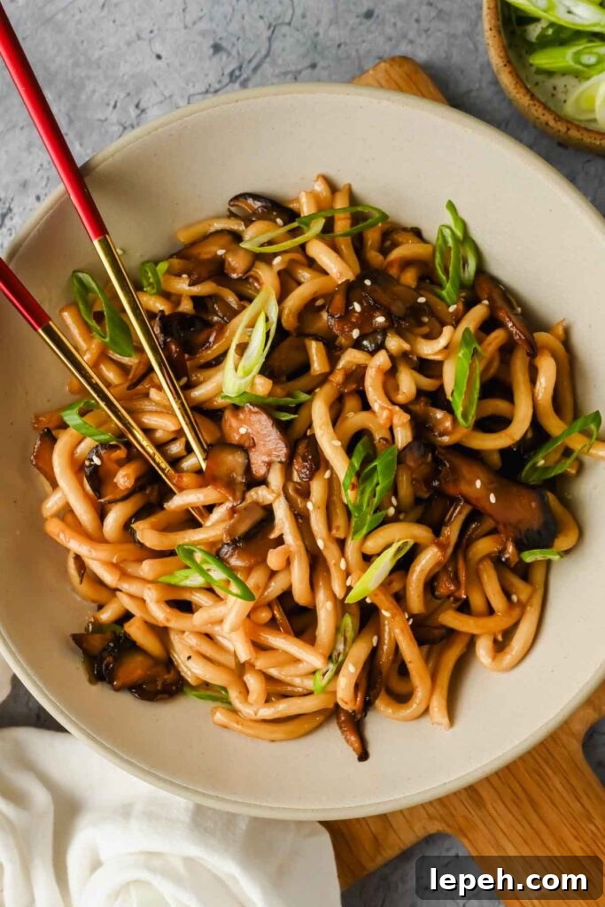 udon noodle and mushroom dish plated on white serving dish garnished with green onion.