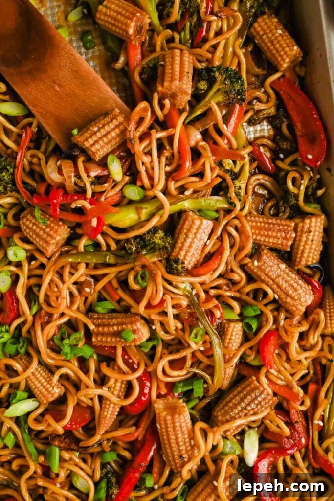 sheet pan chow mein with broccoli, peppers and corn mixed on gold baking sheet.
