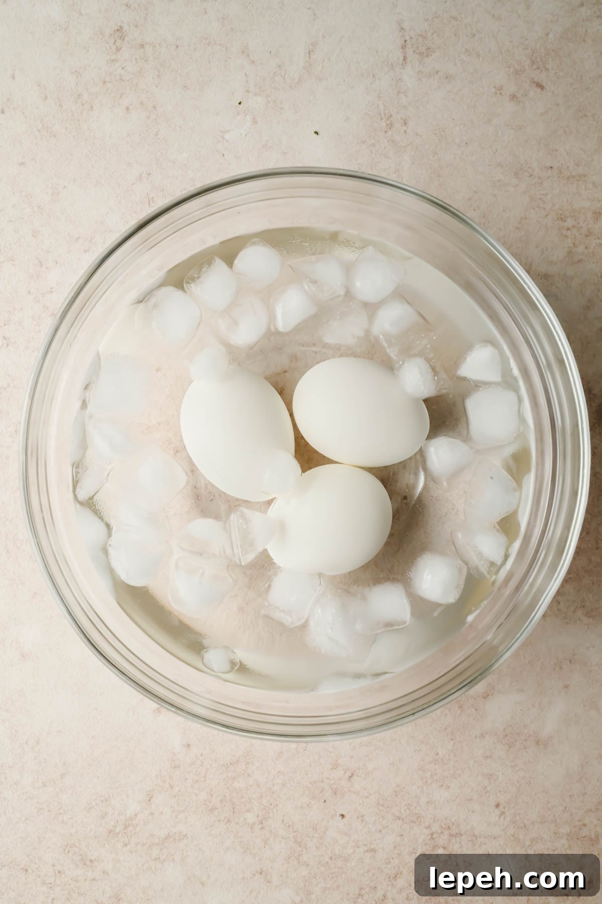 three hard boiled eggs submerged in ice bath in glass bowl.