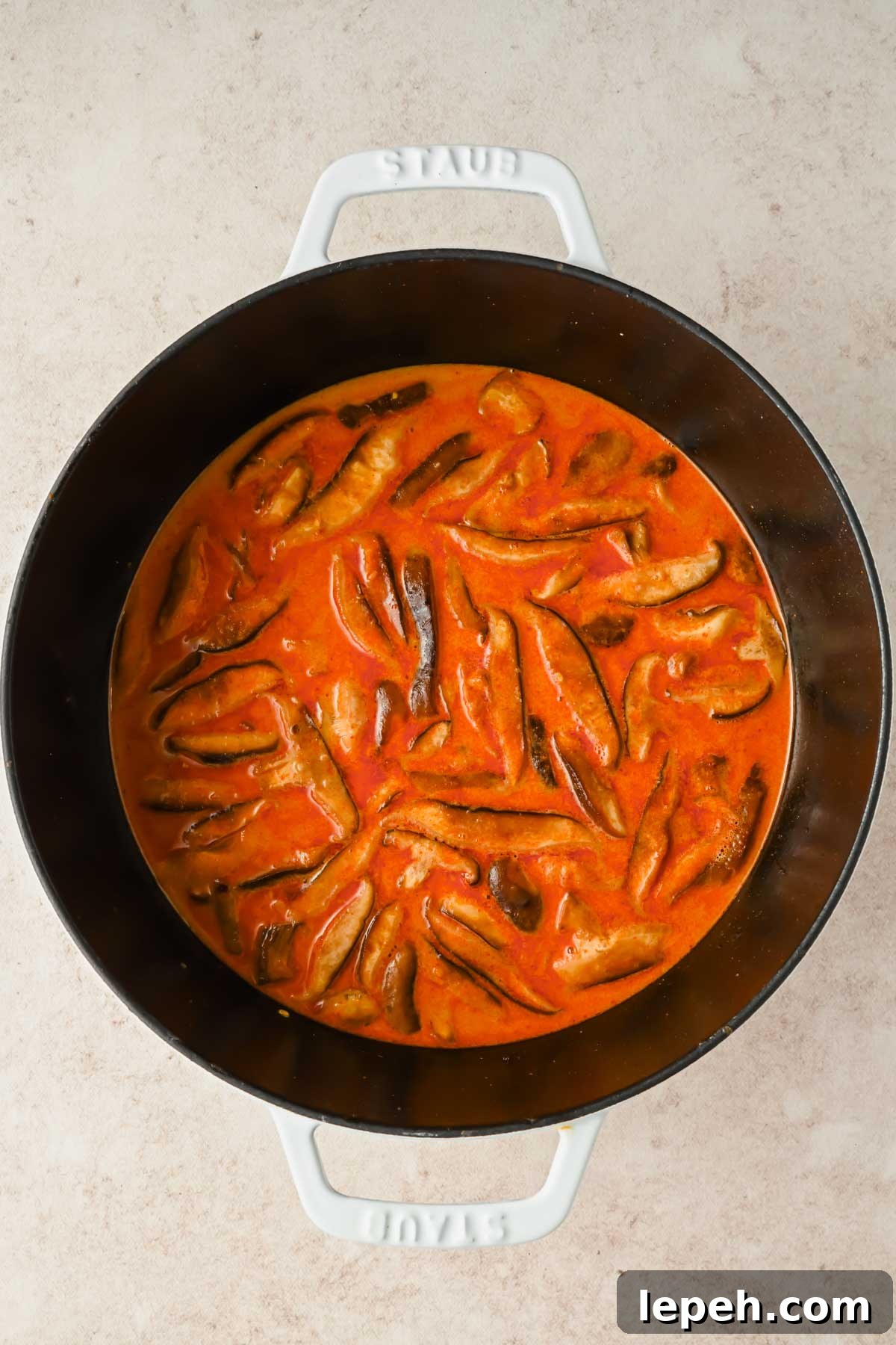 mushrooms cooking in red curry sauce in large pot.