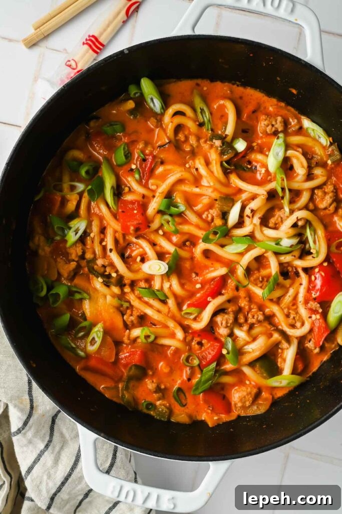 curry udon noodles simmering in large pot topped with sliced scallions.