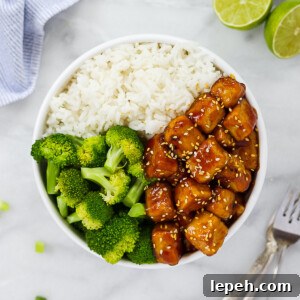 A white bowl holding sesame tofu, white rice, and broccoli.