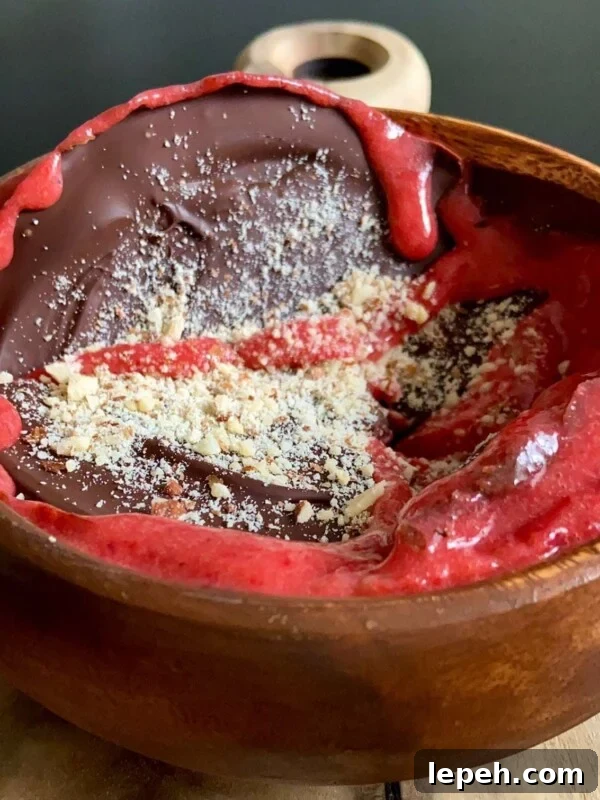 A wooden bowl filled with dark chocolate, bright red berry sauce, and a sprinkle of crushed nuts, resembling a strawberry smoothie bowl.