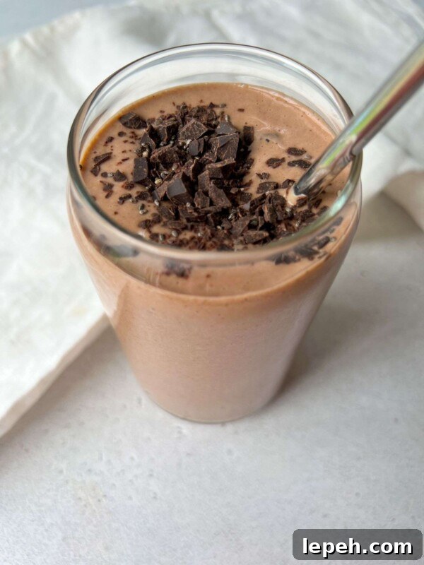 A glass filled with a healthy chocolate smoothie, topped with chopped dark chocolate pieces and a metal straw.