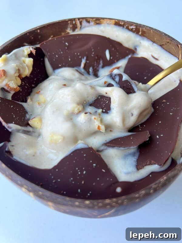 A bowl filled with creamy banana ice cream topped with dark chocolate and chopped nuts, served with a gold spoon.