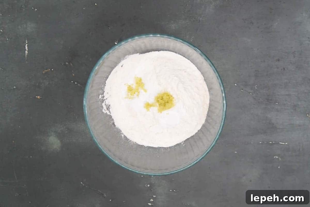 All-purpose flour, baking powder, baking soda, and lemon zest mixed in a bowl.