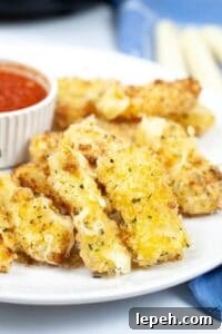 A plate of crispy Air Fryer Mozzarella sticks served with a small bowl of marinara sauce on the side.