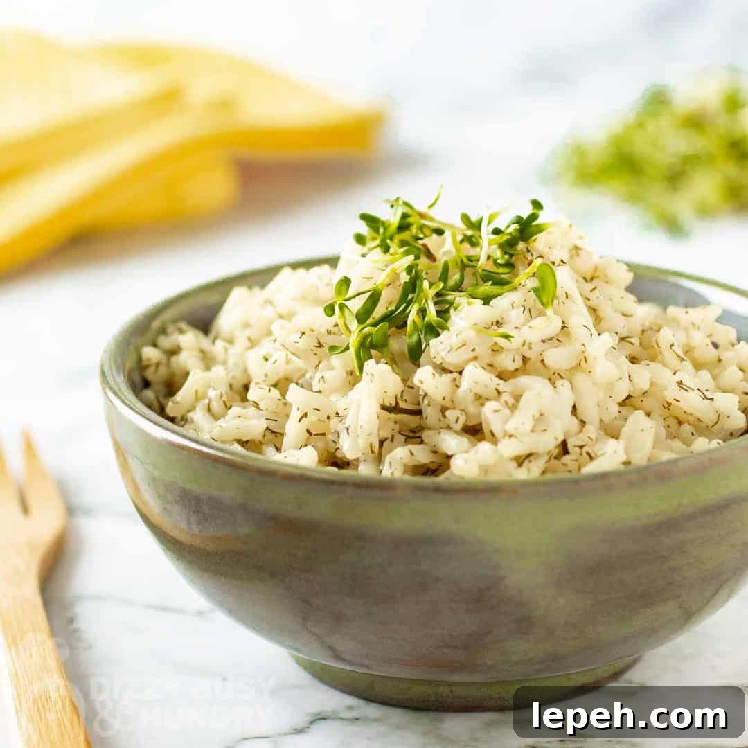 Side view of lemon dill rice garnished with herbs in an olive green bowl on a marble table with a wooden fork on the side.