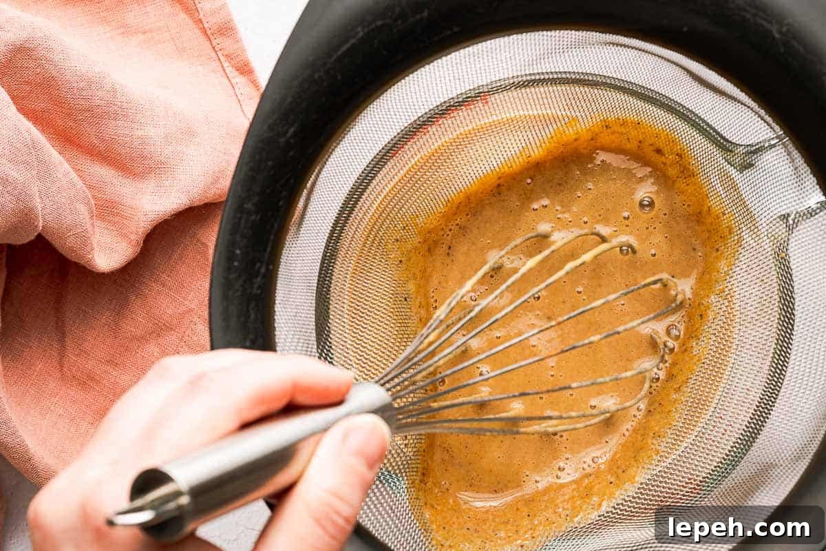 whisk pushing syrup through strainer