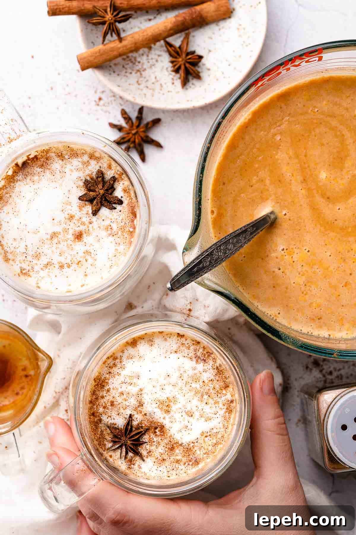 hand holding pumpkin spice latte with cup of pumpkin spice syrup on the side
