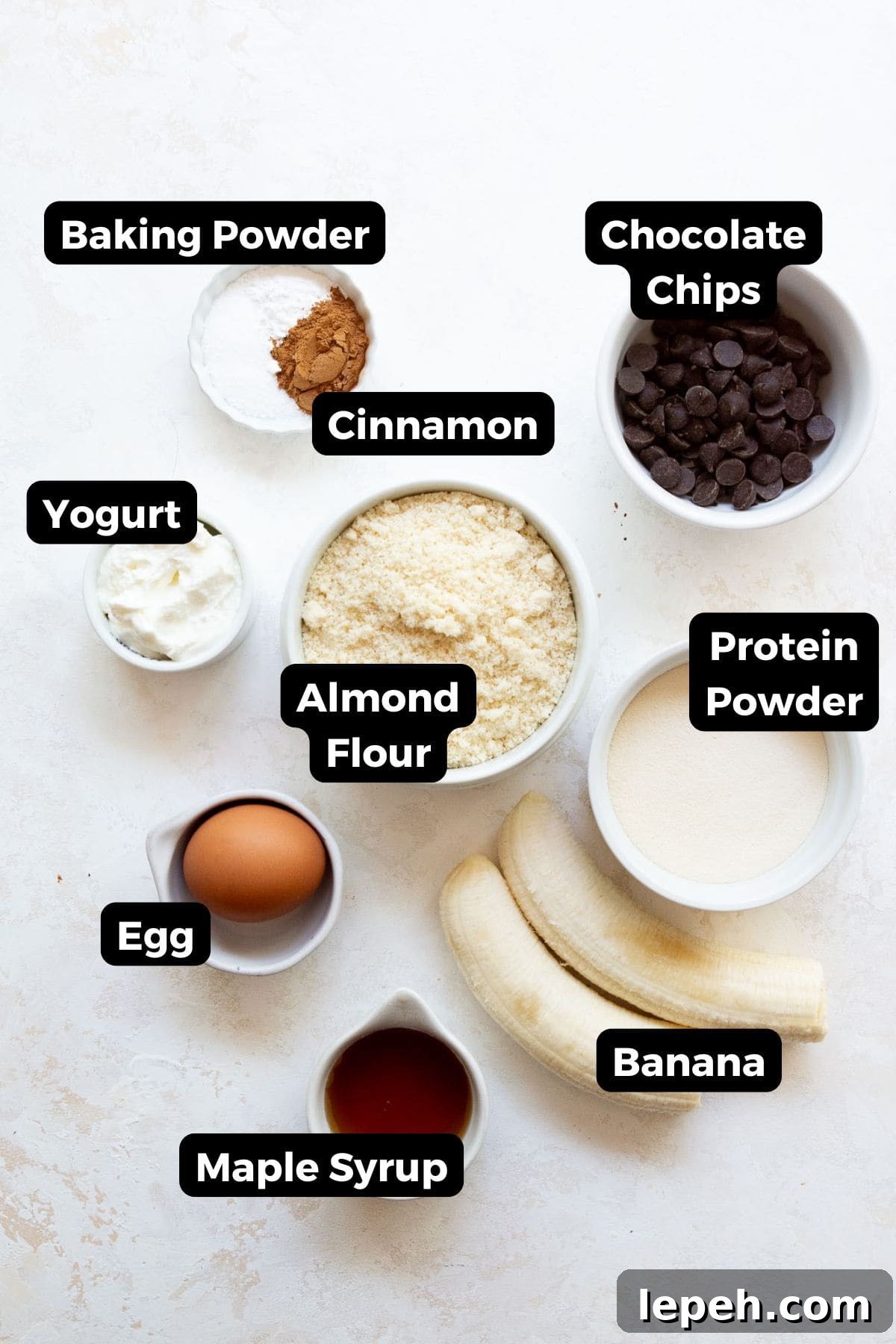 all ingredients in bowls including almond flour, protein powder, egg, yogurt, banana, maple syrup, egg, baking powder, and cinnamon