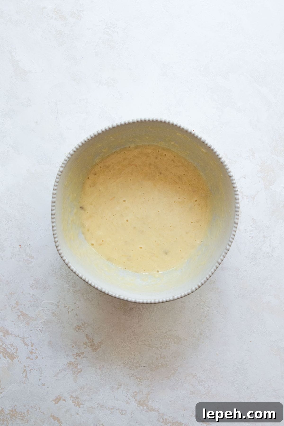 Wet ingredients for banana protein muffins whisked together in a bowl, including mashed bananas, Greek yogurt, egg, and honey.