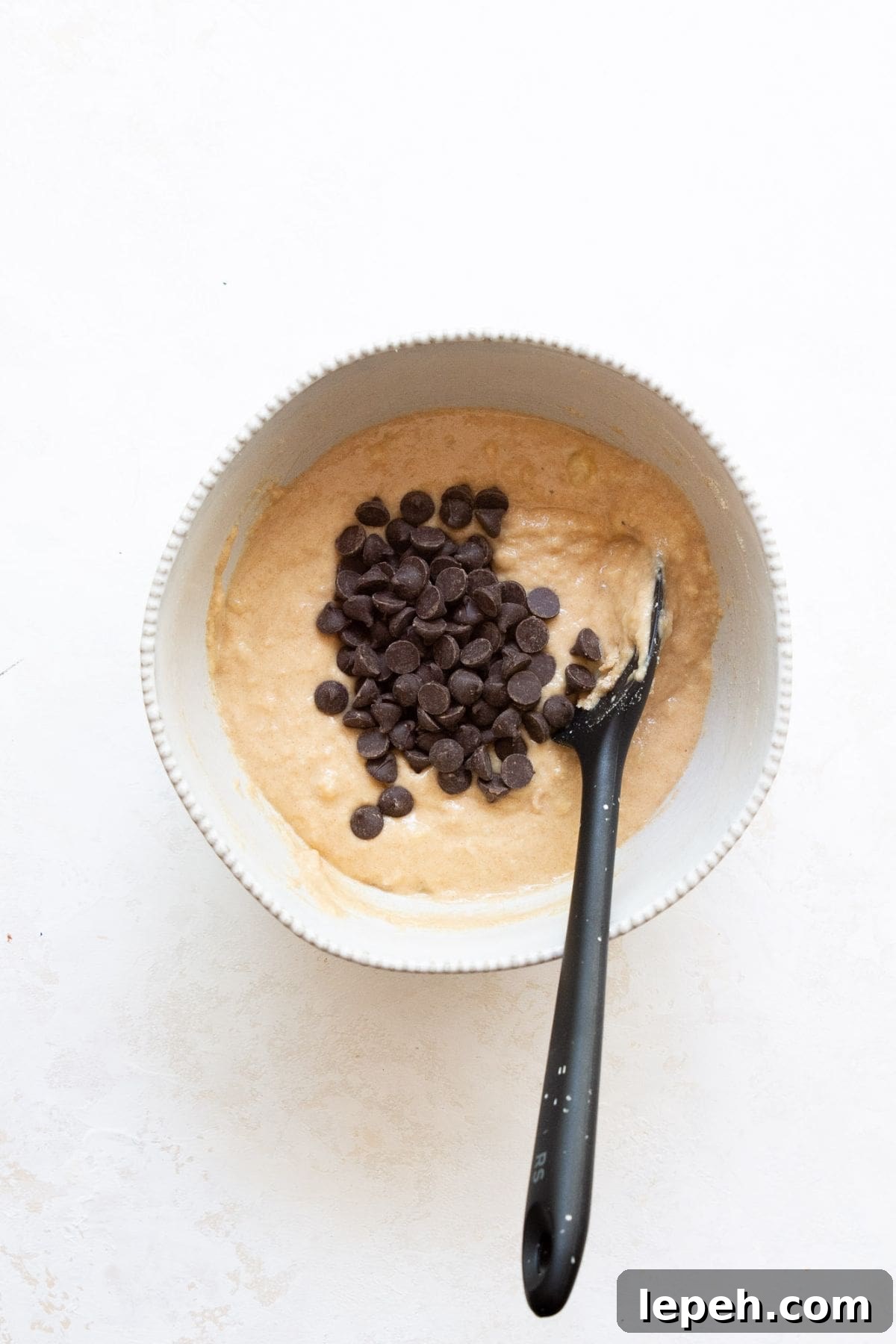 Chocolate chips folded into banana protein muffin batter in a bowl, ready to scoop into the muffin tin.
