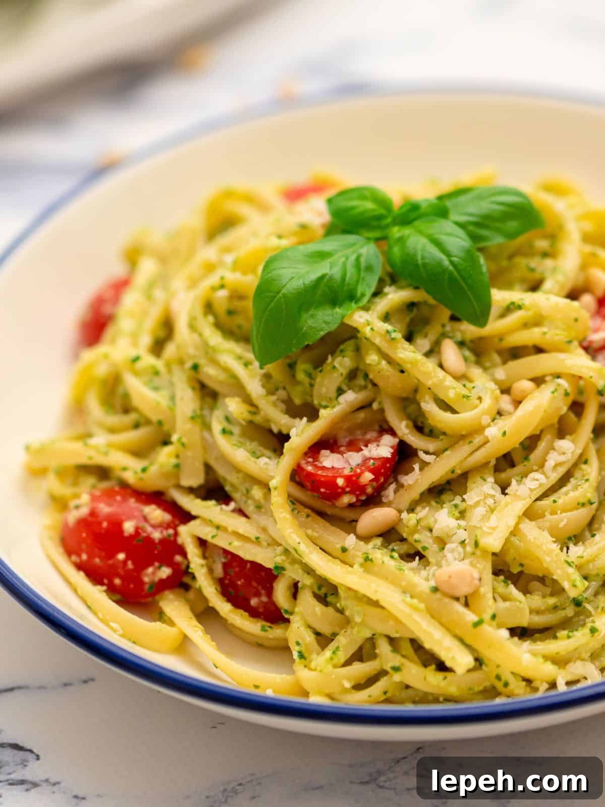 Bowl of pesto pasta tossed with fresh tomatoes and basil.