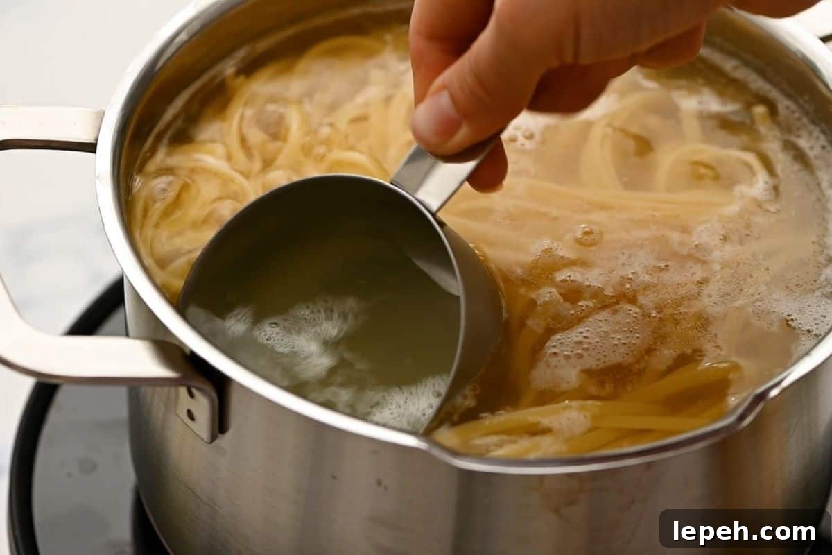 Measuring cup scooping out pasta water from pan cooking linguine.