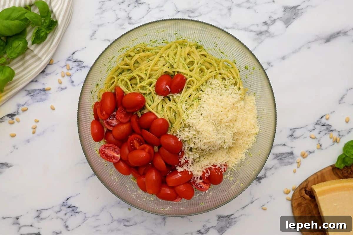 Large mixing bowl with cooked pasta, pesto, tomatoes, and parmesan.