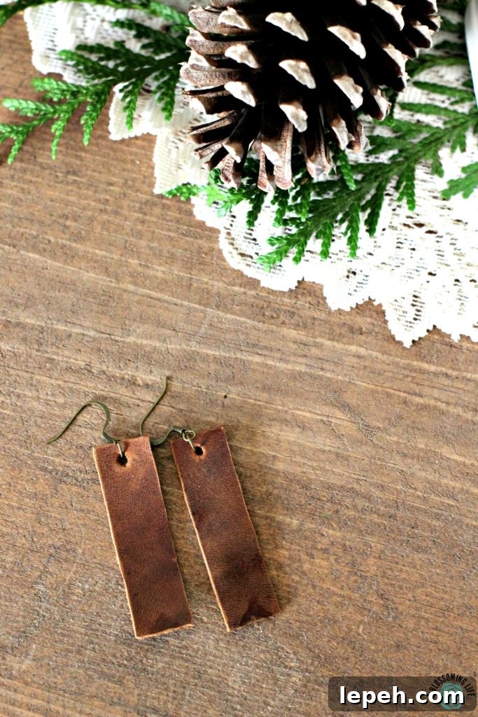 Pair of brown rectangular earrings laying on a table with pine cones on a white fabric doily behind it