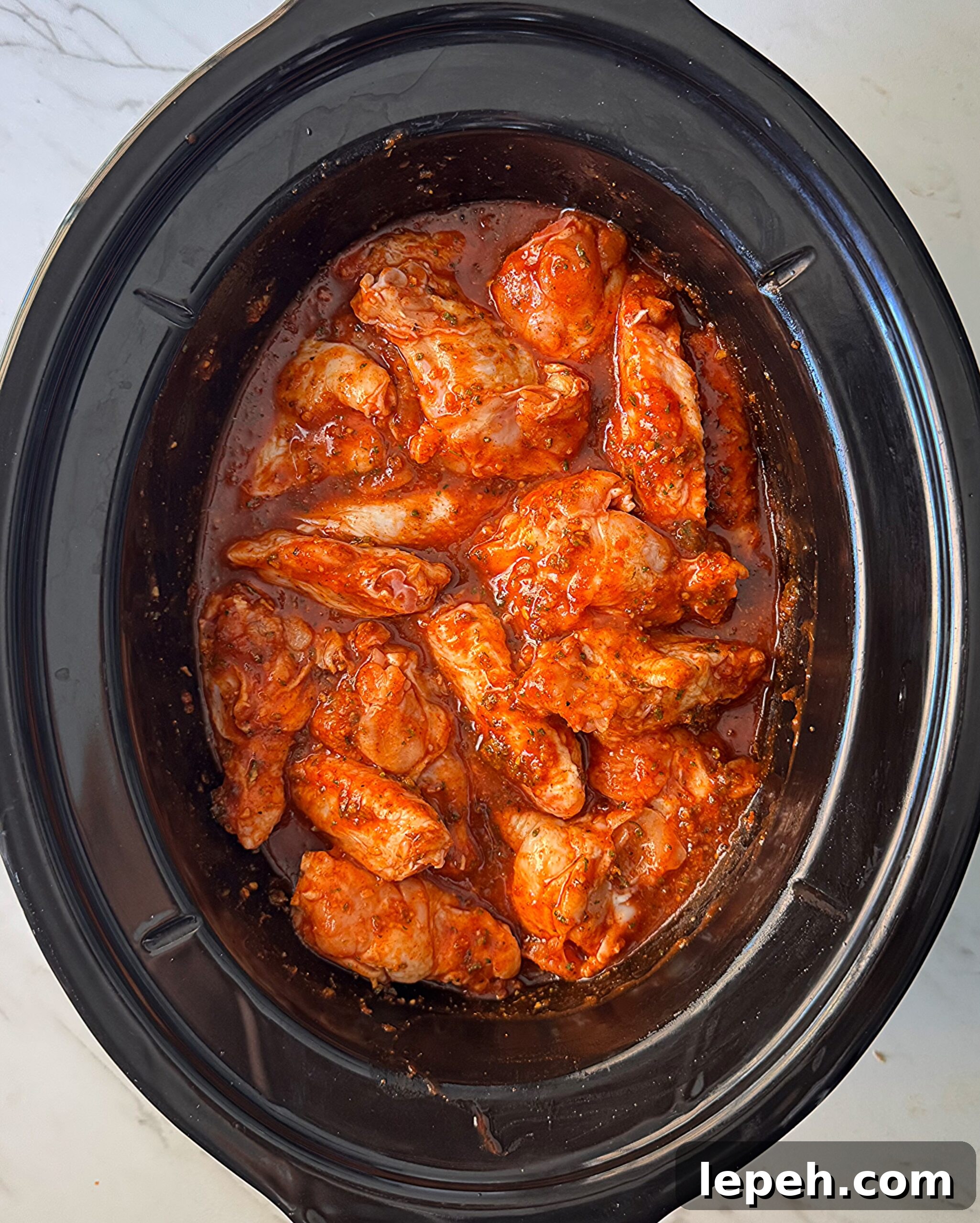 overhead shot of uncooked Buffalo wings in a black slow cooker