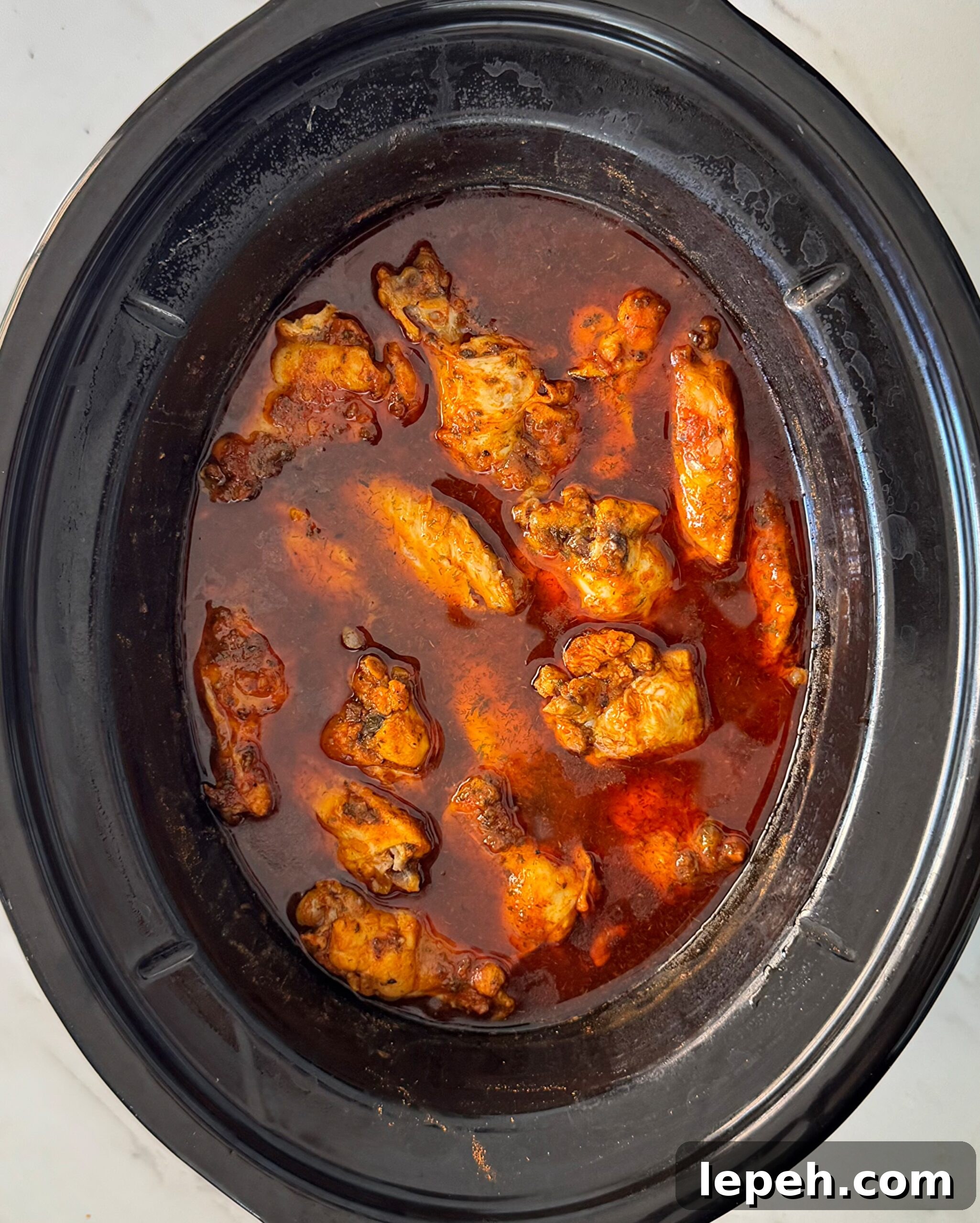 overhead shot of cooked Buffalo wings in a black slow cooker