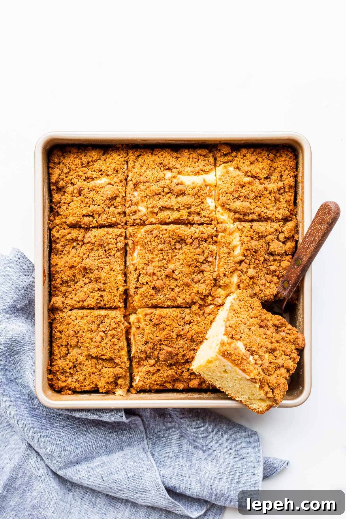 Serving apple crumb cake from a square cake pan with a mini offset spatula.