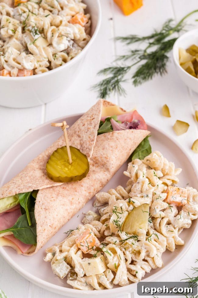 Pickle pasta salad on a white plate alongside a sandwich wrap