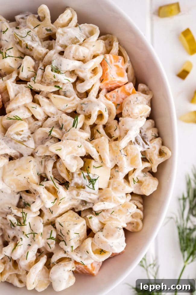 Pasta salad in a white serving bowl with fresh dill next to the bowl.